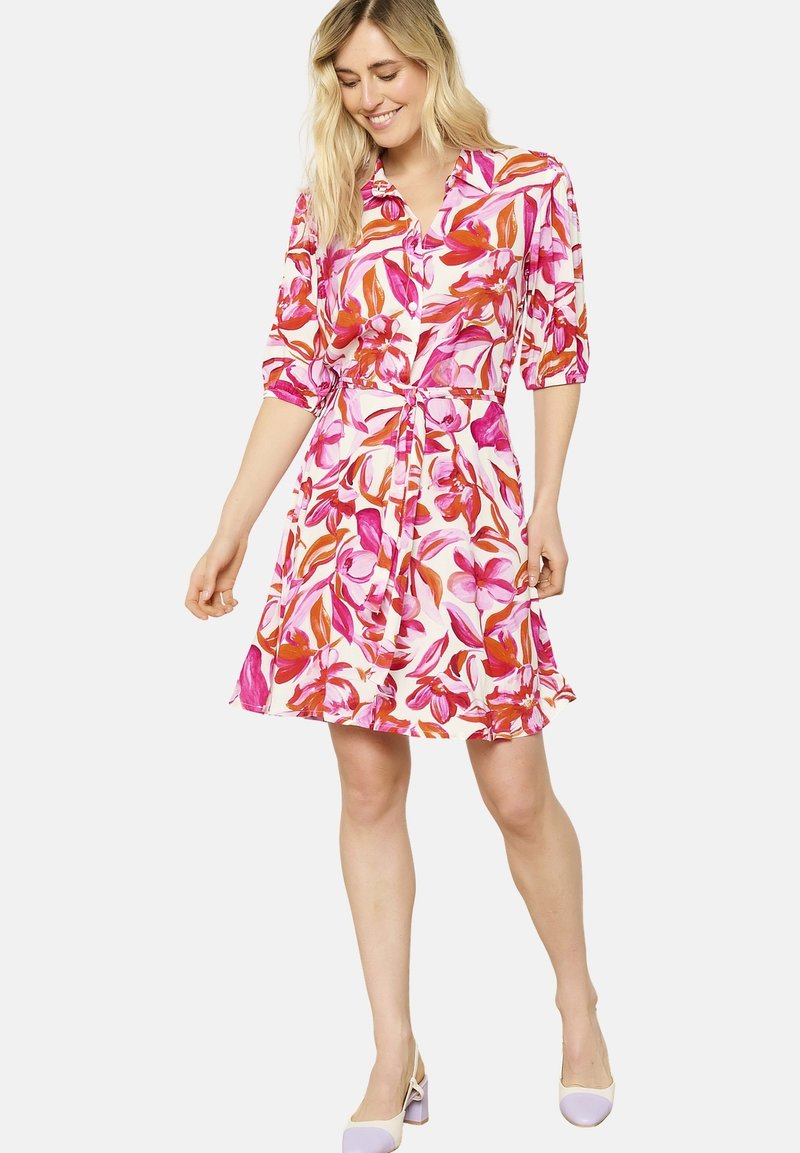 Kukallinen mekko, jossa on vaaleanpunaisia ja oransseja kuvioita, lyhyet puffihihat, kauluspääntie, vyötäröltä kireä ja liehukasa skirt.