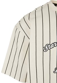 Kortærmet, off-white t-shirt med sorte lodrette striber og "Star" tekst, lavet af blødt bomuldsmateriale. Rund udskæring og løs pasform.