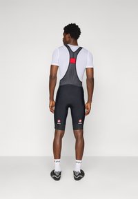 Culotte de cyclisme noire avec des accents rouges et un dos en mesh, associée à une chemise à manches courtes blanche. Comprend un rembourrage au niveau de l'assise.