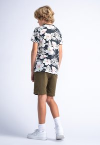 Chemise noire à manches courtes avec des motifs floraux roses et verts, associée à un short olive et des baskets blanches, vue de derrière.