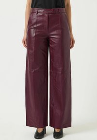Bordeaux leren wijde broek met een hoge taille, voorzien van een gladde textuur en gestikte paneeldetails. Draag met zwarte hoge hakken.