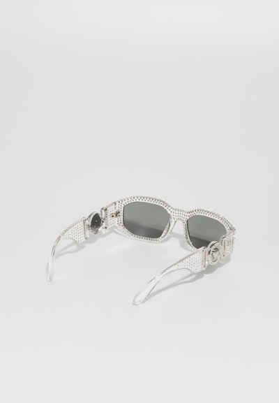 Silver sunglasses with a textured design, dark lenses, and embellished temple detail. Transparent earpieces enhance the overall look.