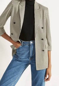 Blazer a scacchi bianco e nero con revers, abbinato a un top nero a coste e jeans blu a vita alta.