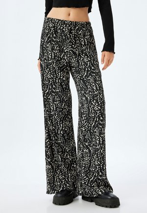 Schwarz-weiß gemusterte weite Hosen aus strukturiertem Stoff, mit einem elastischen Bund und kombiniert mit klobigen schwarzen Schuhen.