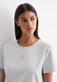 Lichtgrijze katoenen t-shirt met een ronde halslijn en korte mouwen. Heeft een geborduurd logo in het midden van de borst.