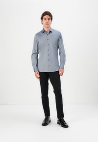 Cămașă albastru deschis, cu un texture subtilă, purtată cu pantaloni negri ajustați și pantofi negri lucioși.