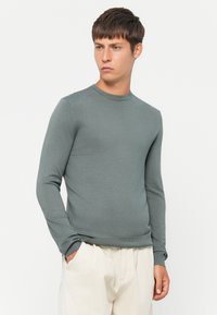 Gray long-sleeve sweater made of soft material, featuring a crew neckline and fitted cuffs, paired with light-colored trousers.