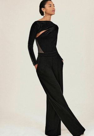 Sorte velour jumpsuit med lange ærmer, der har en snoet halsudskæring og mesh-sidelæg. Bred ben-design med sidelommer.