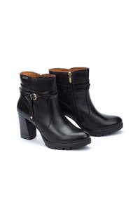 Botas de cuero negras hasta el tobillo con un tacón cuadrado, que presentan una cremallera lateral, una correa decorativa con un hebilla dorada y una suela texturizada para mayor tracción.