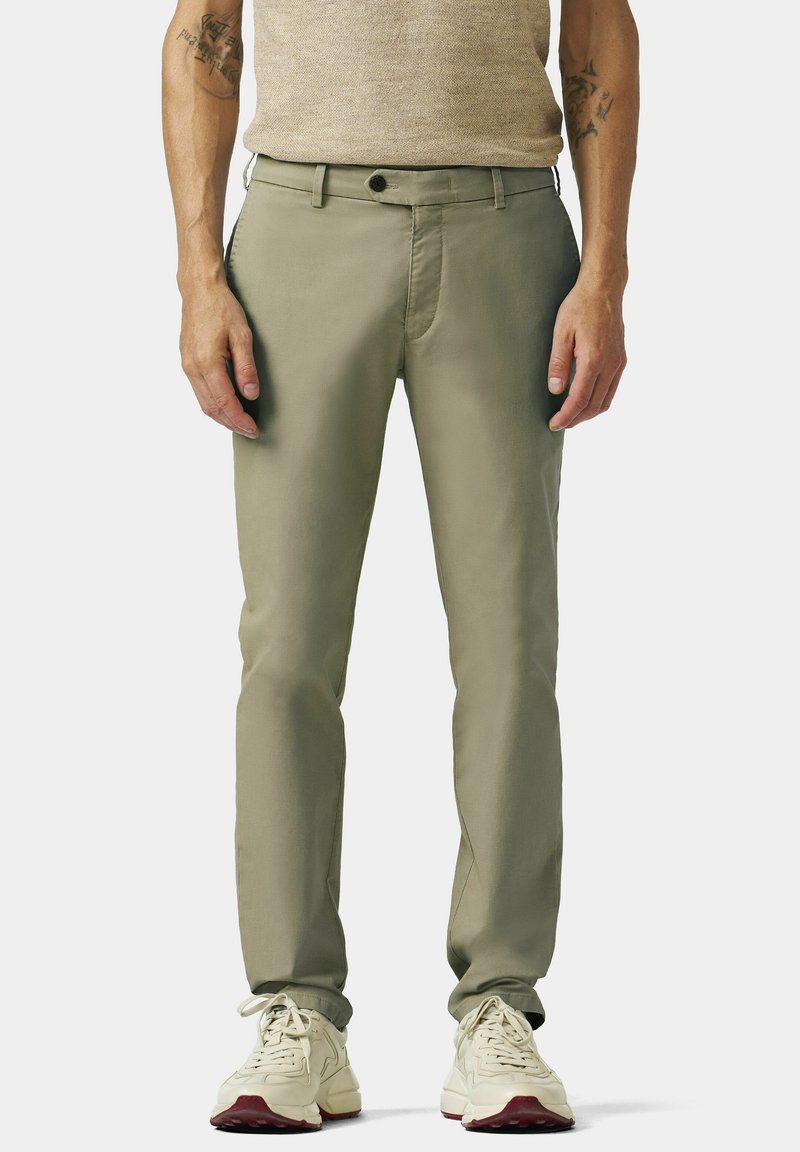 Helle grüne Chinos aus glattem Stoff, mit Fronttaschen und Knopfverschluss. Kombiniert mit beigen Sneakers, die einen lässigen Look kreieren.