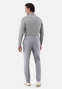 Helles graues Langarmshirt mit weichem Material, kombiniert mit hellgrauen, maßgeschneiderten Hosen. Sichtbare Gesäßtaschen und seitliche Details. Neutrale Schuhe.