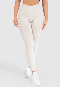 Leggings beige a vita alta realizzati in tessuto elasticizzato, progettati per il comfort. Presentano una vita senza cuciture e una silhouette aderente.