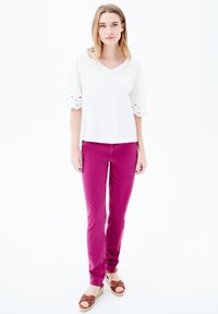 Top bianco a V con ritagli sagomati sulle maniche, abbinato a pantaloni slim rosa acceso e scarpe espadrillas marroni. Design semplice e moderno.