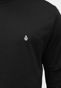 Μαύρο βαμβακερό μπλουζάκι με κοντά μανίκια και στρογγυλή λαιμόκοψη. Διαθέτει μικρό λευκό κεντητό λογότυπο στο αριστερό στήθος. Λεία υφή.