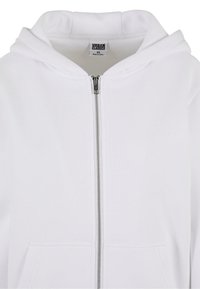 Felpa con zip bianca realizzata in morbido tessuto, dotata di cappuccio standard, tasche frontali e una cerniera argentata. Etichetta con la scritta "URBAN CLASSICS, XS."