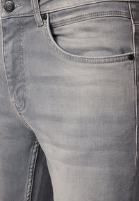 Zbliżenie na jasnoszare dżinsy pokazujące szczegóły przedniej kieszeni, szlufki na pasek, guzika i szwów.