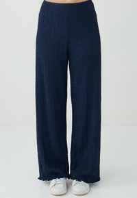 Marineblauwe wijde broek gemaakt van textiel met een gekreukeld ontwerp, voorzien van een elastische tailleband en een rafelige zoom, gecombineerd met witte sneakers.