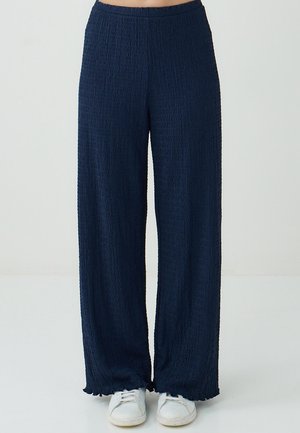 Navy wide-leg pants made of textured fabric with a crinkled design, featuring an elastic waistband and frayed hem, paired with white sneakers.