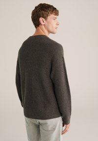 Siv časa pleten pulover s teksturo, spuščena ramena in sproščen fit. Kombinira se s svetlo obarvanimi jeans hlačami. Prikazana je zadnja stran.