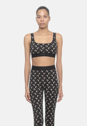 Reggiseno sportivo nero e leggings con un motivo a mezzaluna ripetuto in beige. Entrambi presentano un ampio elastico con branding.