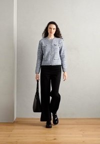 Gray knit cardigan with two chest pockets and buttons, paired with black wide-leg pants and black shoes, holding a black handbag.