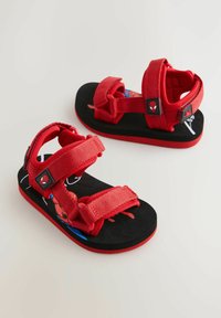 Röda sandaler med justerbara tygremmar, en svart texturerad sula och en Spiderman-grafik på fotbädden. Designade för komfort och stöd.