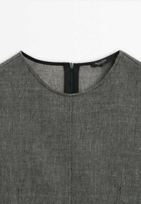 Robe grise texturée avec un col rond, fermeture éclair au dos et un contraste de bord noir le long des bords.