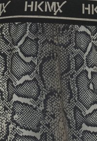 Svart och grått ormskinnstrykt tyg med en texturerad yta. Har en svart midjeresår med "HKMX"-logotyp högst upp.