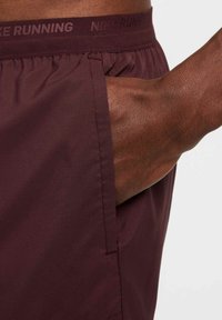 Nike juoksushortsit syvässä burgundin värissä, kevyestä ja teksturoidusta kankaasta, elastinen vyötärönauha logolla ja sivutaskut.