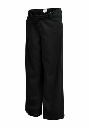 Donna che indossa pantaloni neri a vita alta e un maglione corto nero che mostra una piccola area di pelle alla vita.