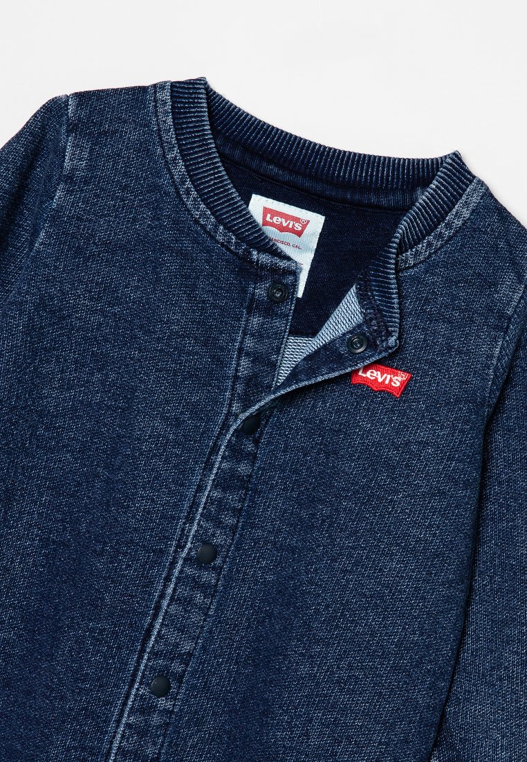 Dunkelblaue Jeansjacke mit Knopfleiste, geripptem Kragen und schwarzen Knöpfen. Mit einem roten Levi's Logo-Etikett am Halsausschnitt.