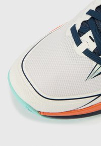 Avant de chaussure de course blanc et bleu marine avec semelle bleu sarcelle et accent orange, avec dessus en mesh et lacets bleu marine sur fond blanc.