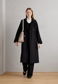Must mustriga kahe nööbiga mantel laia kraega, kantud musta sviitriga ja valge särgi üle; kokku sobitatud mustade pükstega ja beeži õlakotiga.