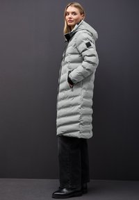 Ljusgrå vadderad jacka med en huva, med dragkedjestängning, sidofickor och en slät yta. Buren över svarta jeans och ankelboots.