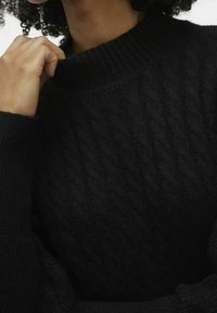 Pull noir en tricot torsadé avec un col montant à côtes et un motif texturé. Le tissu semble doux et épais avec un aspect confortable.