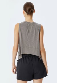 Top grigio senza maniche con orlo asimmetrico, realizzato in un tessuto morbido e testurizzato. Abbinato a pantaloni corti neri con vita elastica.