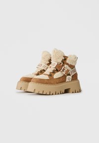 Botas de plataforma tan gruesas con forro de borreguillo beige, suelas gruesas beige, cordones y correas de marca alrededor de los tobillos.