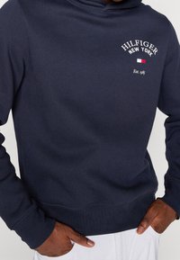 Felpa con cappuccio blu navy realizzata in morbido misto cotone, con tasca a marsupio, polsini a costine e stampa del logo bianco sul petto.