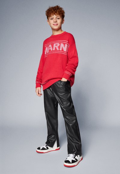 Röd stickad tröja med texten "WARM", svarta byxor i konstläder och svartvita sneakers med röda sulor. Enkel, avslappnad outfit.