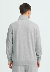 Sweat-shirt gris en polaire avec un col montant, des poignets et un ourlet côtelés. Le dos est uni avec une coupe décontractée, adapté pour une tenue casual.