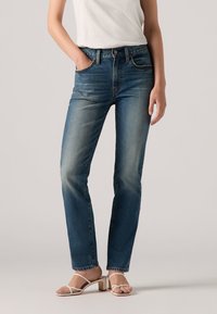 Lichtblauwe jeans met een vervaagde afwerking, recht gesneden ontwerp, vijf pockets stijl en een metalen knoopsluiting, gecombineerd met witte bandjes sandalen.