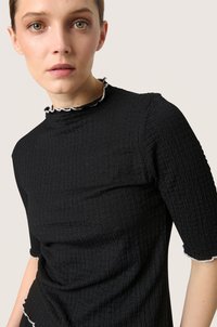 Sort tekstureret top med høj krave og bølget hvid kant. Korte ærmer, tætsiddende design med et rynket stofmønster.