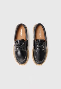 Schwarze Lederschuhe mit runder Zehenform, Schnürdesign, brauner Innensohle und kontrastierenden Nähten. An der Innensohle ist das Logo der Marke Pineapple sichtbar.