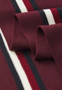 Primo piano di un tessuto a maglia bordeaux piegato con strisce verticali in nero, bianco e rosso, che mostra dettagli di texture e trama.