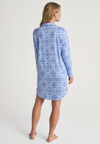 Camicia da notte blu a maniche lunghe con un motivo geometrico bianco, dotata di colletto e orlo leggermente curvo, realizzata in tessuto morbido.