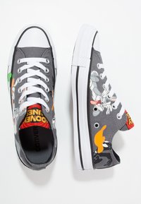 Sneakers in tela grigia con lacci bianchi, caratterizzati da disegni di personaggi dei cartoni animati. Suola in gomma con accenti neri e una fodera interna patterned.