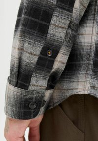 Camisa de franela de cuadros en tonos grises y beige, con botones negros y puños relajados de acabado suave y textura blanda.