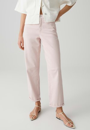 Vrouw draagt lichtroze rechte jeans met beige gestripte puntige platte schoenen en een cropped wit jasje met korte mouwen.