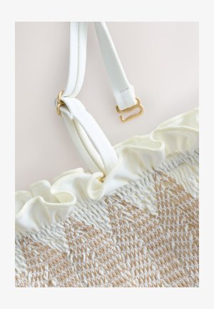 Biely texturovaný textil s volánovým okrajom a béžovým prešívaním, vybavený nastaviteľnými bielymi ramienkami so zlatými háčikmi a krúžkami.