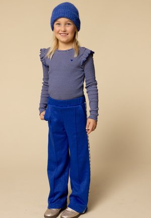 Blauw gestreept longsleeve shirt met flounces, gecombineerd met glanzende blauwe wijde broek met zijstrepen, en een blauwe gebreide beanie. Zilveren schoenen.